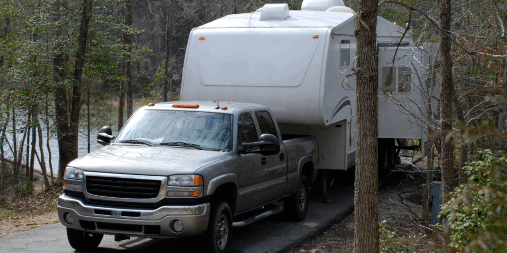 an pickup truck towing a 5th wheel camper through the woods after putting a RV liability insurance policy in place.