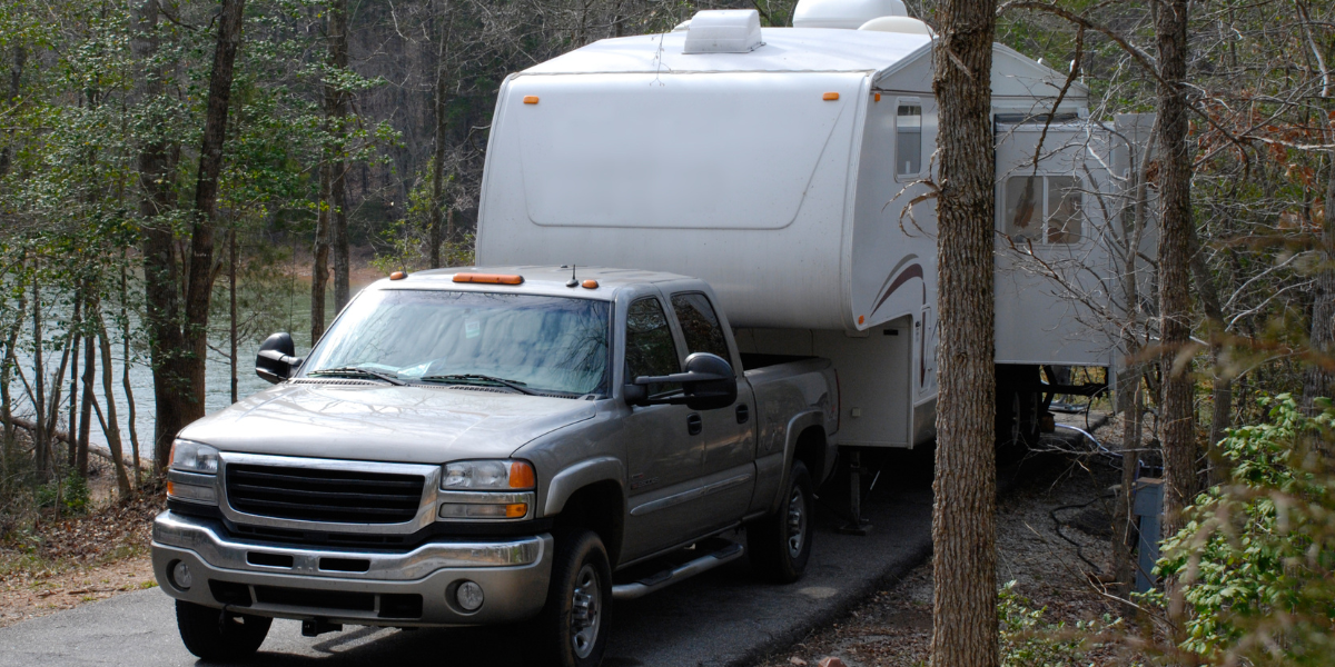 an pickup truck towing a 5th wheel camper through the woods after putting a RV liability insurance policy in place.